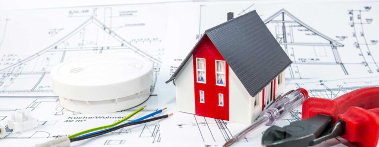 Für die Elektroplanung erforderlich: eine technische Zeichnung. Dargestellt werden außerdem ein Modell vom Haus, Elektrokabel, eine Lüsterklemme, ein Brandmelder und Werkzeug.