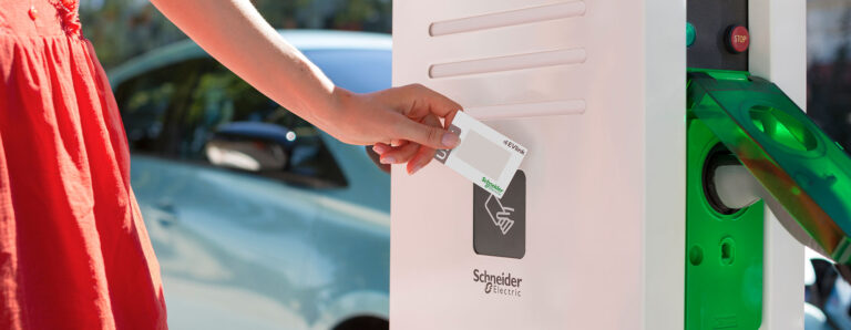 Eine Frau läd ihr E-Auto mit Strom. Sie hält ihre Karte zum Bezahlen an die Ladestation.